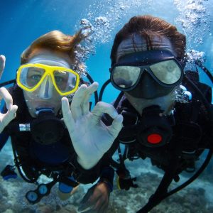 Underwater shoot of a young couple diving with scuba in a tropical sea and showing ok signal